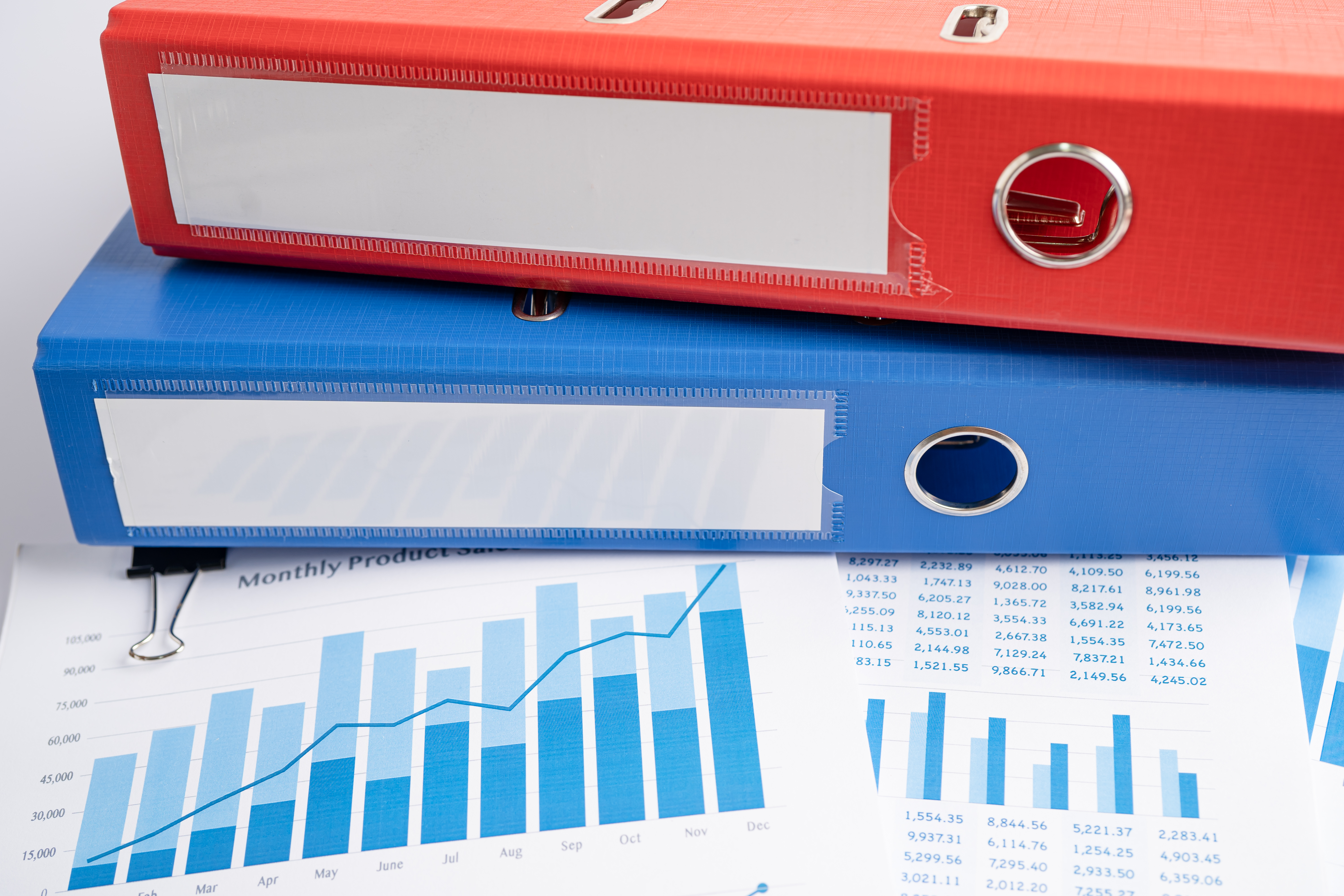 Blue and red binders piled on top of charts showing financial data
