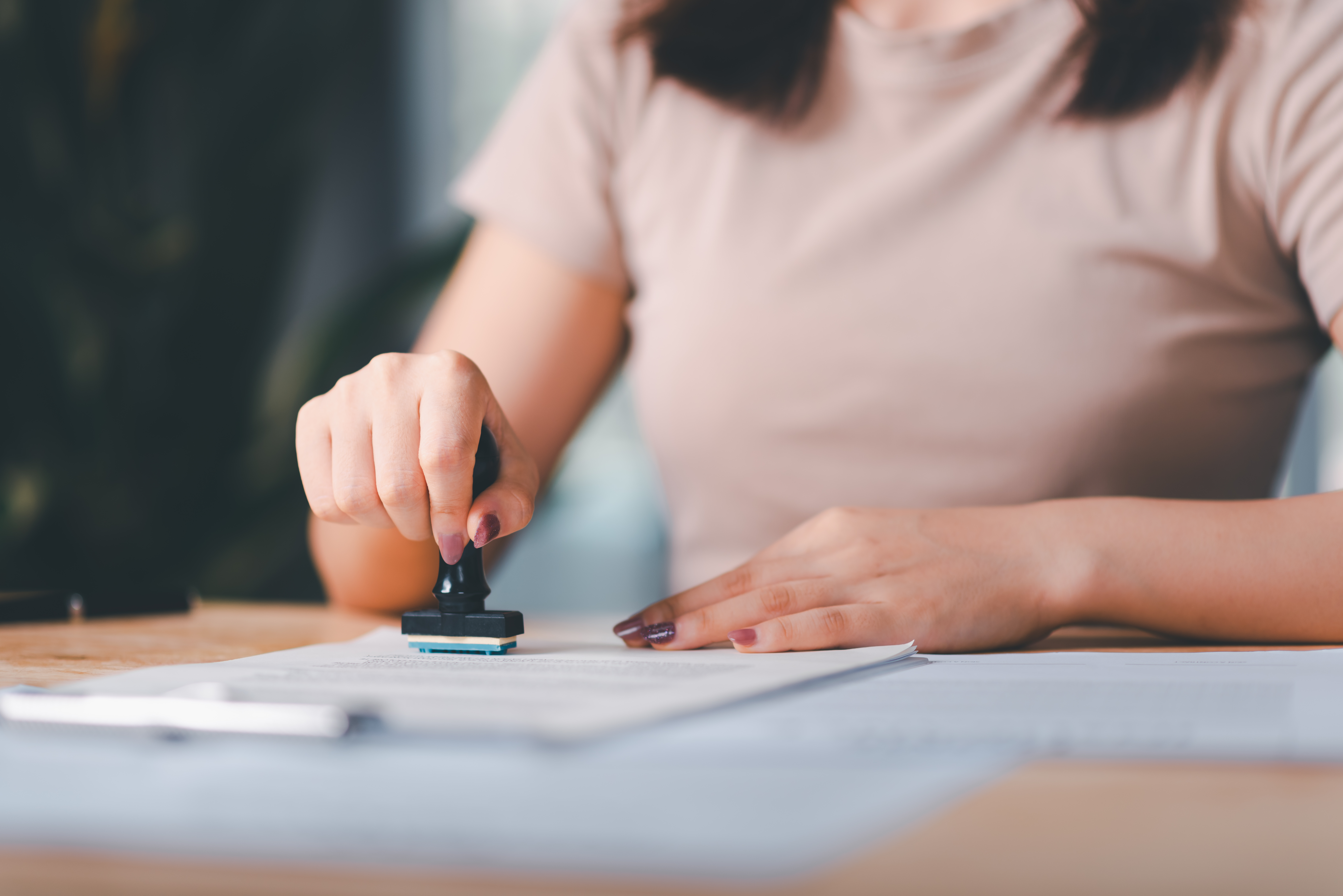 Unseen individual with pink shirt stamping a document with right hand
